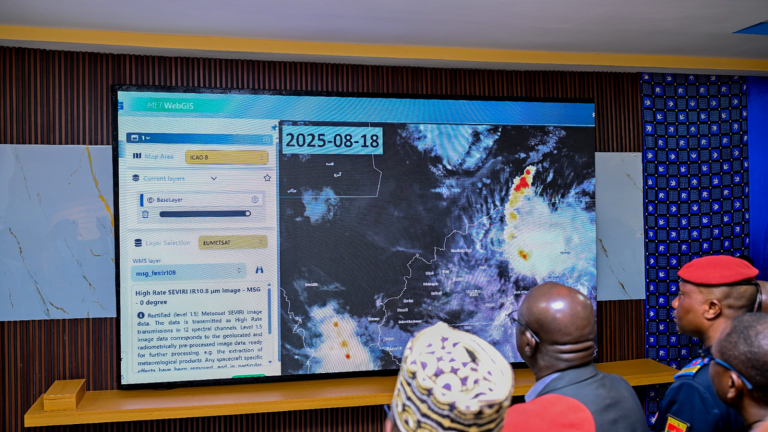 Several uniformed individuals look at a large digital screen displaying weather satellite data and maps dated 2025-08-18.