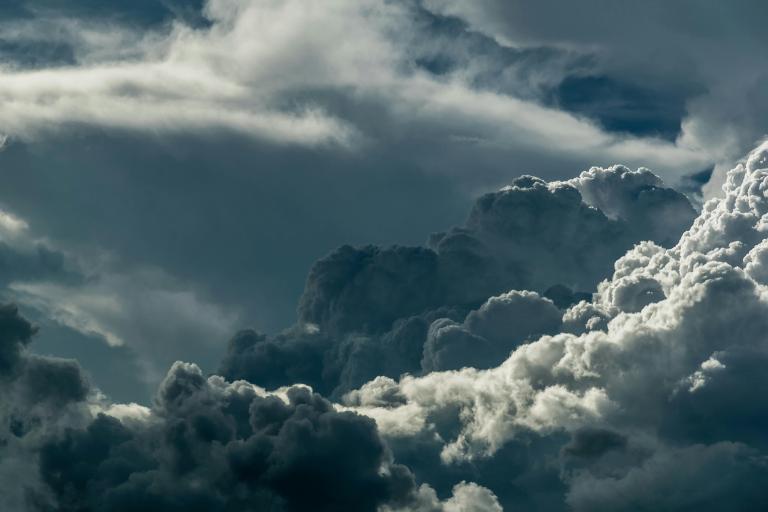 Dark, dense clouds fill the sky with patches of sunlight highlighting their edges, suggesting an approaching storm or unsettled weather.