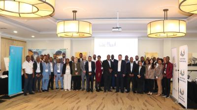 A large group of people pose for a photo in a conference room with banners and presentation screens in the background.