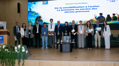 A group of people in business attire stand on stage in front of a screen displaying a French presentation about youth involvement in early warning systems.