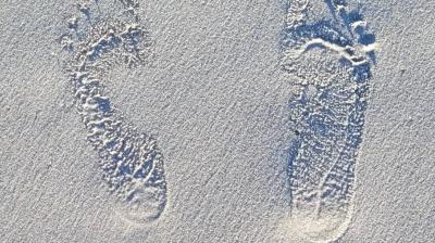 Two barefoot footprints are pressed into smooth, pale sand, with visible toe and heel marks.