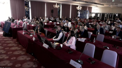Delegates seated at rows of tables with maroon tablecloths during an international conference.