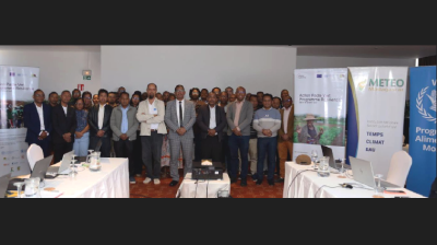 A group of people standing in a conference room in front of promotional banners for Meteo Madagascar and an environmental program.