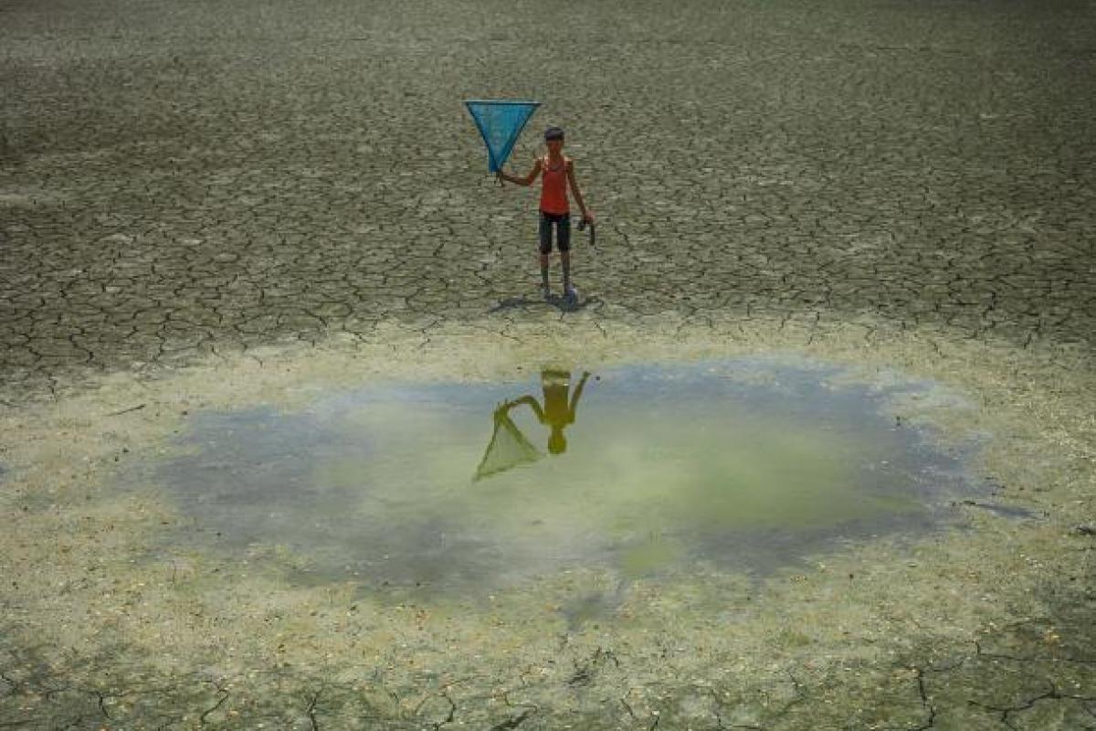 Child standing near a dry lake holding a kite