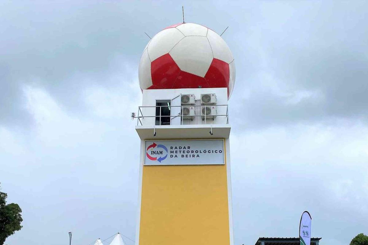 A tall structure with a large radar dome painted to resemble a red and white soccer ball is labeled "Radar Meteorológico da Beira" against a cloudy sky.