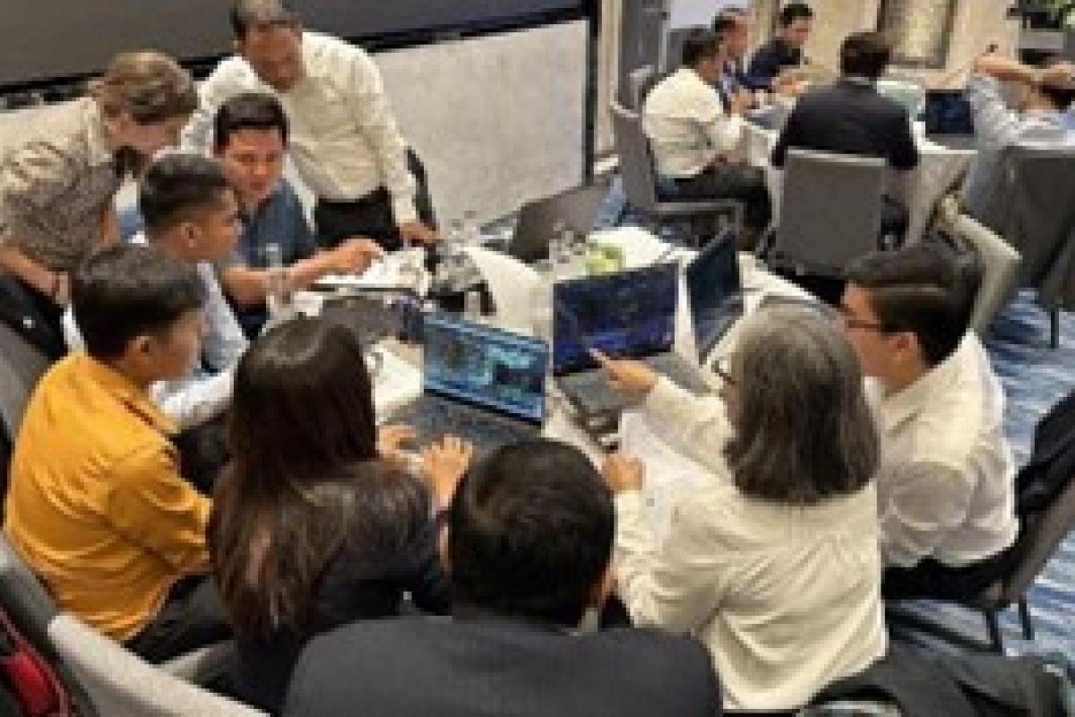 A group of people sit around a table with laptops, engaged in discussion.