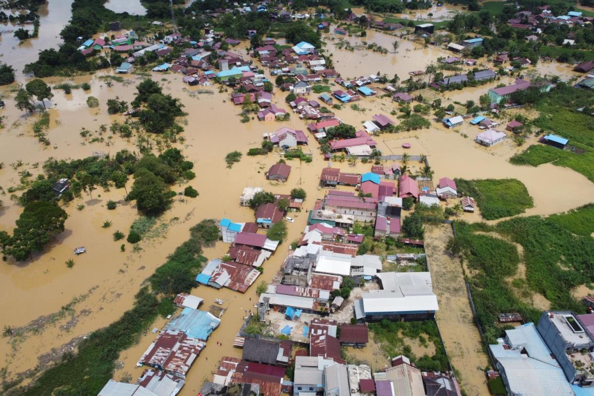 Aerial view of a town with many buildings partially submerged in floodwaters, surrounded by muddy water and patches of greenery.