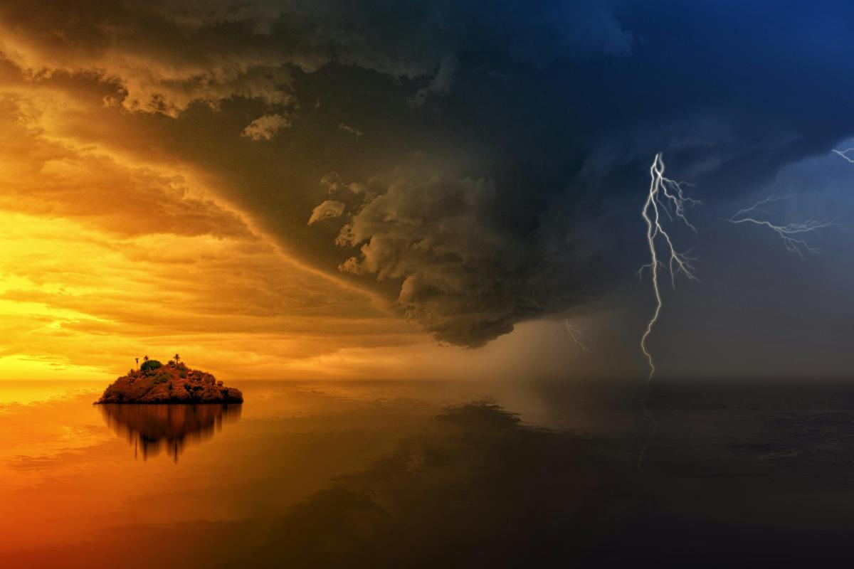 A small island sits on calm water under a dramatic sky split between a bright sunset and a dark storm with lightning.
