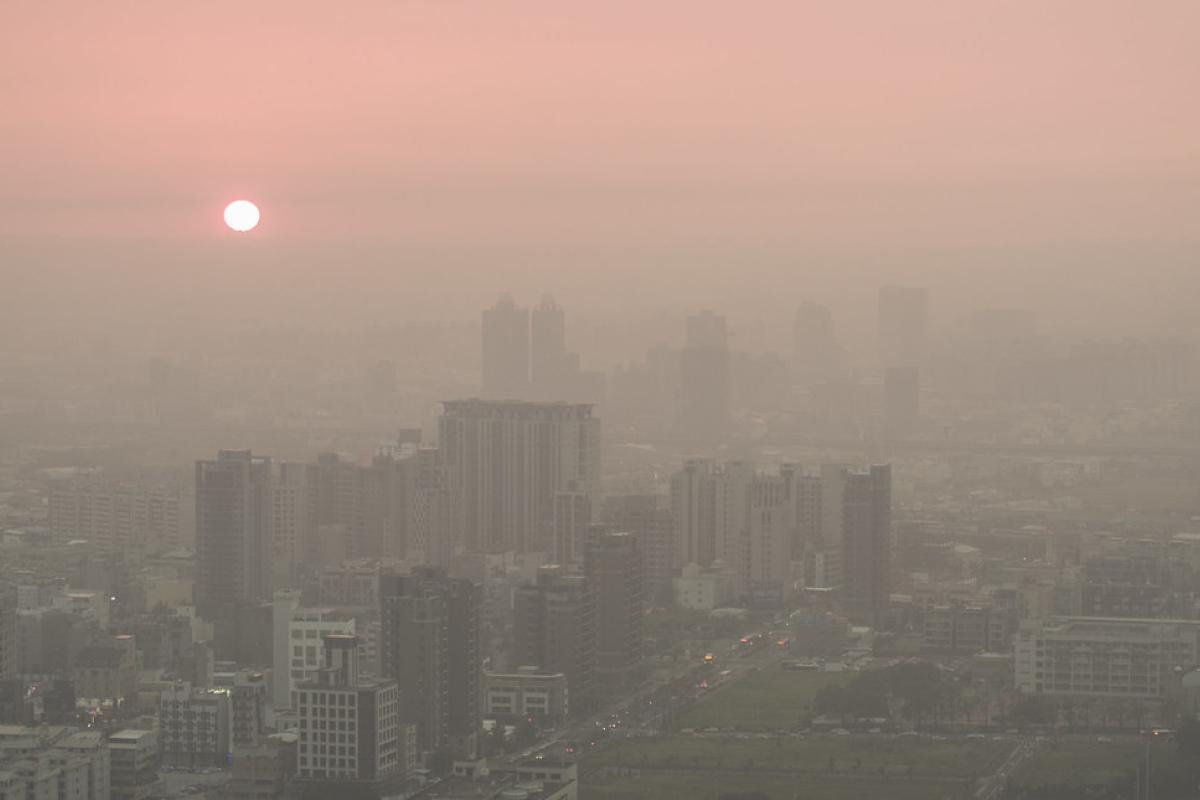 Air pollution in Taiwan. The sun sets over a city skyline, with high-rise buildings and heavy smog creating a hazy, pink-tinged atmosphere.https://www.flickr.com/photos/cslmedia888/30677065680