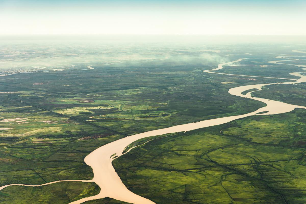 Aerial view of a wide, winding river flowing through green farmland and fields under a hazy sky.